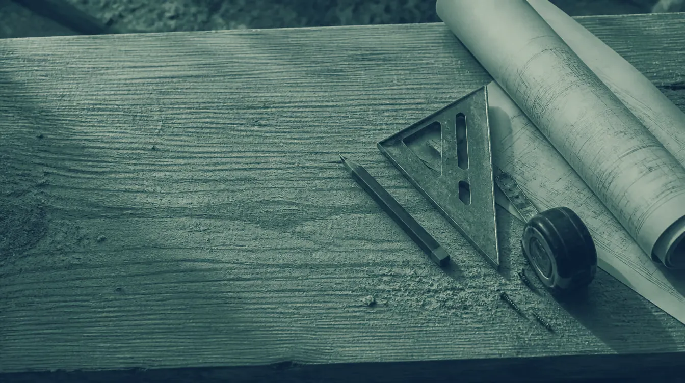 A framing square, pencil, tape measure and rolled drawings on a fir plate