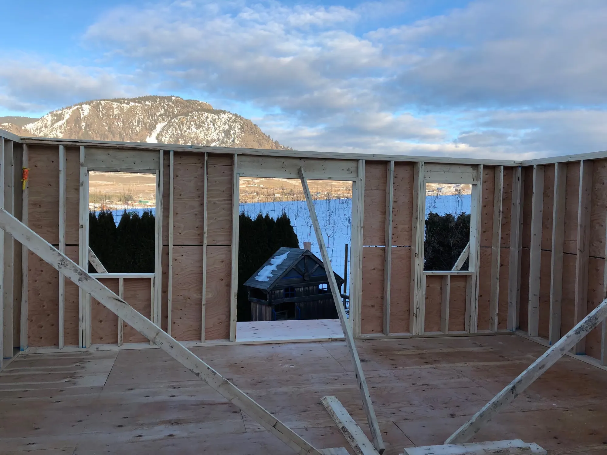 A rough framed window opening in a house under construction, looking out over Okanagan Lake and the mountains beyond